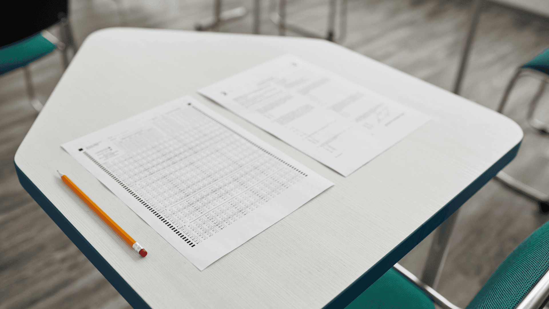 An empty school classroom desk with a standardized test bubble sheet, a question booklet, and a pencil resting on top.