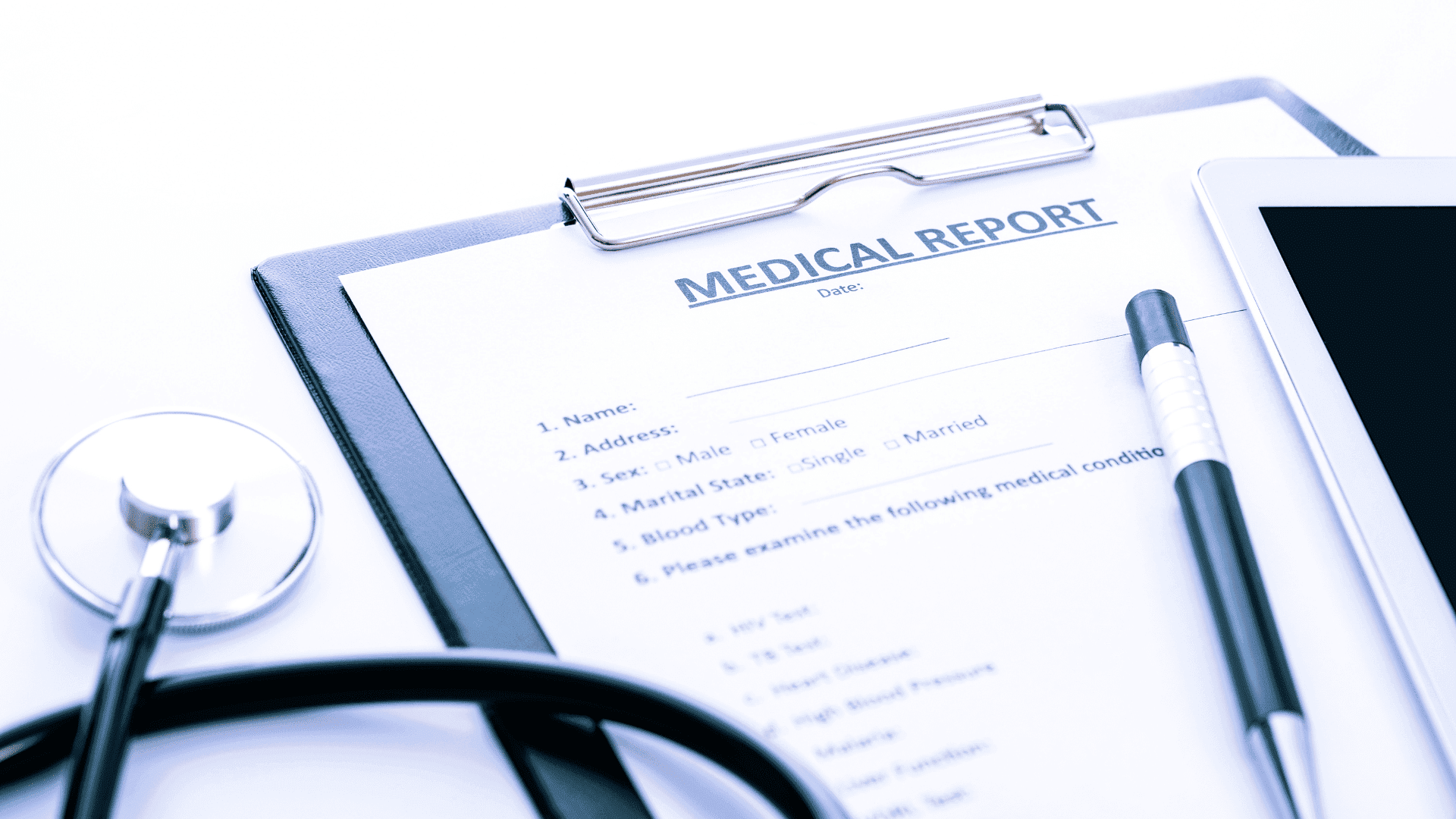 Medical report form on a clipboard next to a pen, tablet, and stethoscope for a Social Security Disability claim.