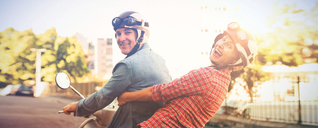 Happy mature couple riding a scooter in the city on a sunny day