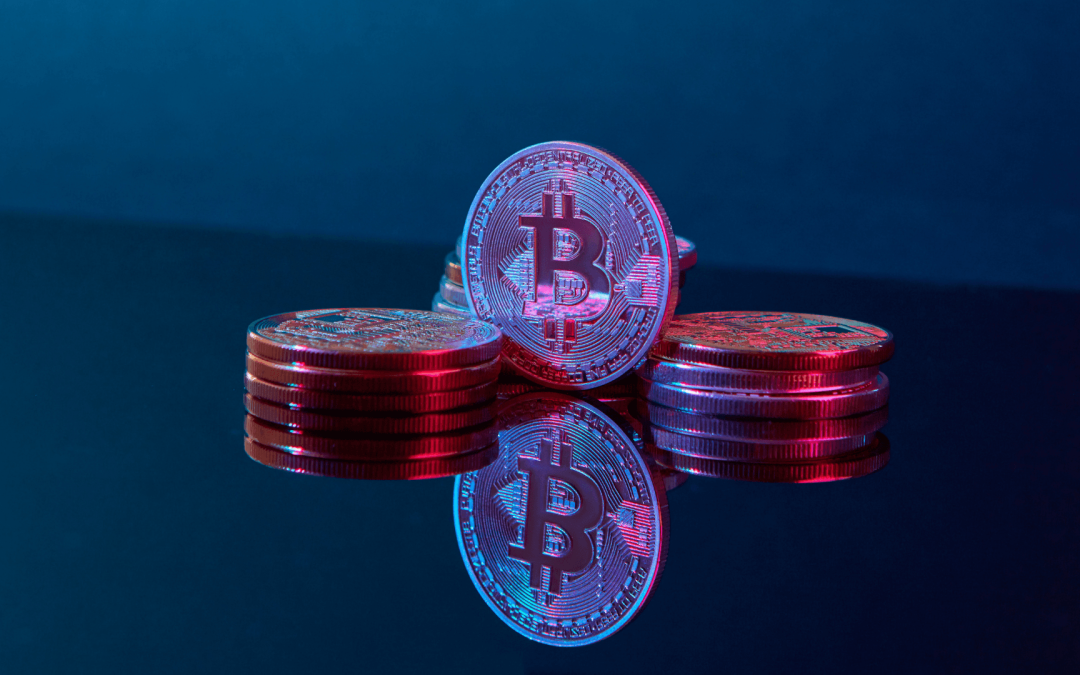 Physical Bitcoin tokens stacked on a reflective dark surface with vibrant blue and pink neon lighting.