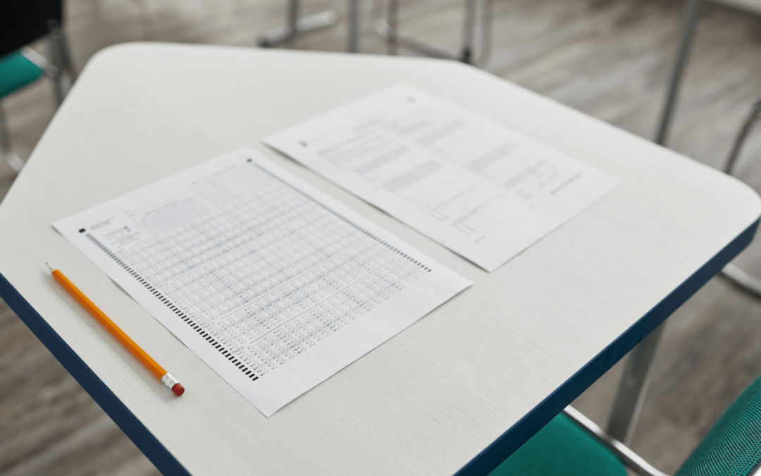 An empty school classroom desk with a standardized test bubble sheet, a question booklet, and a pencil resting on top.
